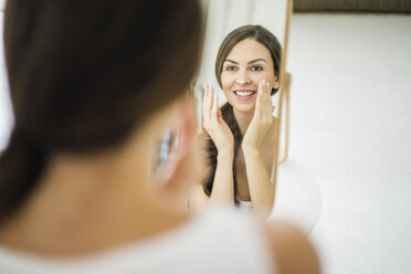 Porträt einer Frau, die ihr Spiegelbild am Morgen betrachtet und sich das Gesicht eincremt - MOEF00202