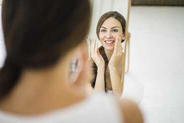 Portrait of woman looking at her mirror image in the morning creaming her face - MOEF00202