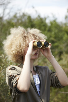 Junge Frau mit lockigem Haar schaut durch ein altes Fernglas - TSFF00140