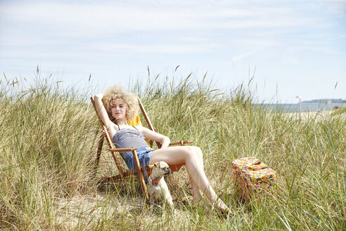 Porträt einer jungen Frau, die auf einem Strandkorb in den Dünen sitzt und etwas beobachtet - TSFF00147