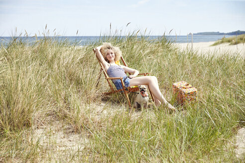Glückliche junge Frau sitzt auf einem Strandkorb in den Dünen - TSFF00148