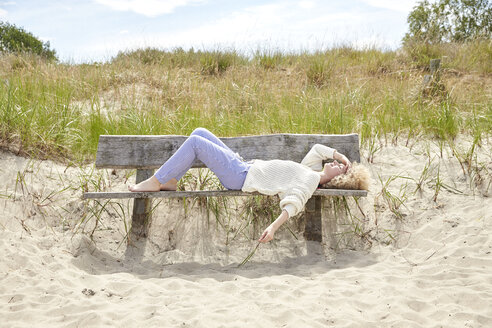 Junge Frau entspannt sich auf einer Bank in den Stranddünen - TSFF00155