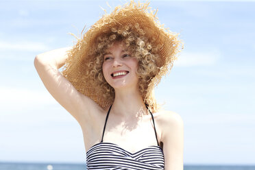 Porträt einer glücklichen jungen Frau mit Strohhut am Strand - TSFF00156