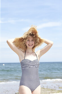 Porträt einer lachenden jungen Frau mit Strohhut am Strand - TSFF00158