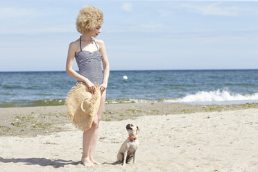 Junge Frau im Badeanzug mit Strohhut und Hund am Strand - TSFF00160