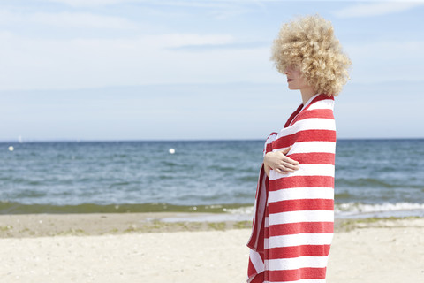 Junge Frau in Strandtuch eingewickelt vor dem Meer stehend, lizenzfreies Stockfoto