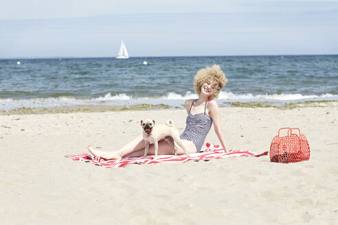 Glückliche junge Frau entspannt sich mit ihrem Hund am Strand - TSFF00165