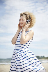 Porträt einer jungen blonden Frau mit Kopfhörern am Strand - TSFF00169