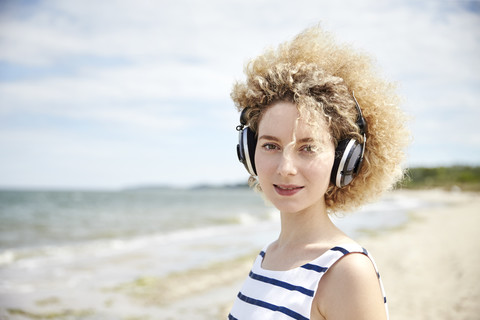Porträt einer jungen blonden Frau mit Kopfhörern am Strand, lizenzfreies Stockfoto