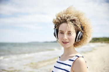 Porträt einer jungen blonden Frau mit Kopfhörern am Strand - TSFF00171