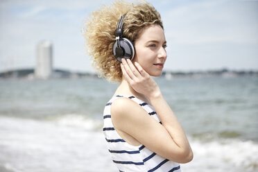 Porträt einer jungen blonden Frau mit Kopfhörern am Strand - TSFF00172
