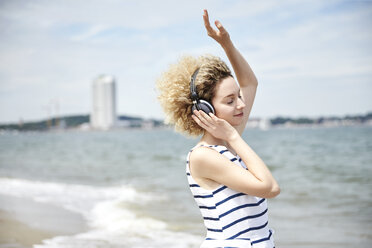 Porträt einer jungen blonden Frau mit Kopfhörern am Strand - TSFF00173
