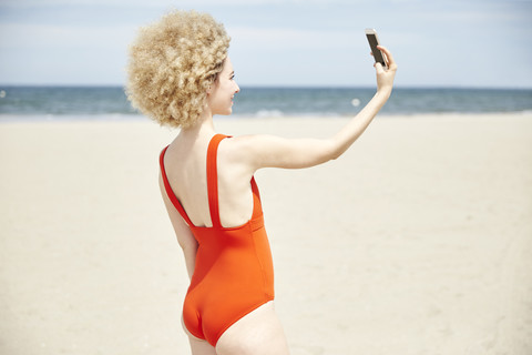 Junge Frau mit lockigem blondem Haar nimmt Selfie am Strand, lizenzfreies Stockfoto