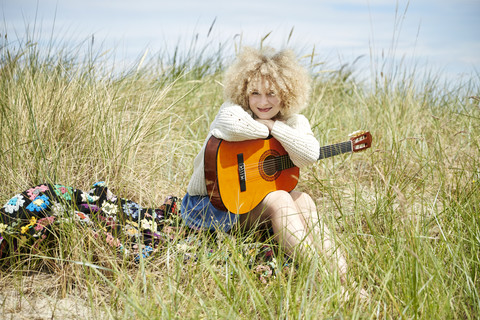 Porträt einer jungen Frau mit Gitarre, die sich in den Stranddünen entspannt, lizenzfreies Stockfoto