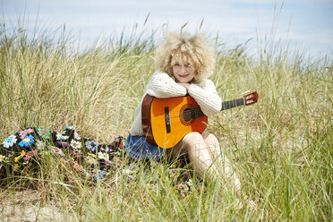 Porträt einer jungen Frau mit Gitarre, die sich in den Stranddünen entspannt - TSFF00188