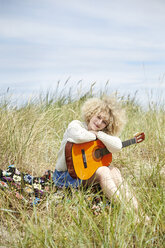 Porträt einer jungen Frau mit Gitarre, die sich in den Stranddünen entspannt - TSFF00189