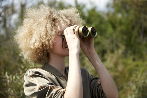 Junge Frau mit lockigem Haar schaut durch ein altes Fernglas - TSFF00200