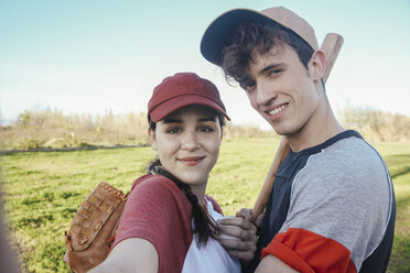 Porträt eines lächelnden jungen Paares mit Baseballausrüstung im Park - RTBF01093