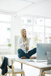 Glückliche Geschäftsfrau sitzt auf dem Schreibtisch im Büro - MOEF00215