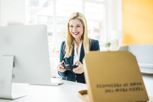 Smiling businesswoman using controller at desk in office - MOEF00222