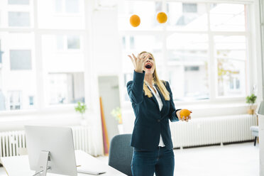 Sorglose Geschäftsfrau jongliert mit Orangen im Büro - MOEF00227