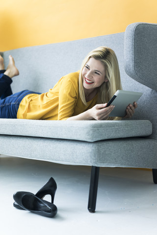 Happy woman lying on couch using tablet stock photo