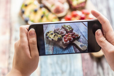 Girl photographing with her smartphone, various sandwiches on chopping board - SARF03399