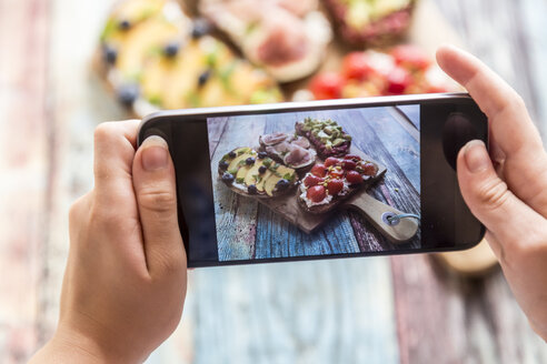 Mädchen fotografiert mit ihrem Smartphone, verschiedene Sandwiches auf Schneidebrett - SARF03399