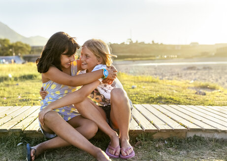 Zwei beste Freunde sitzen an der Strandpromenade und umarmen sich - MGOF03664