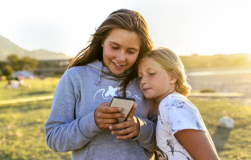 Zwei Mädchen schauen auf ein Handy im Freien - MGOF03678