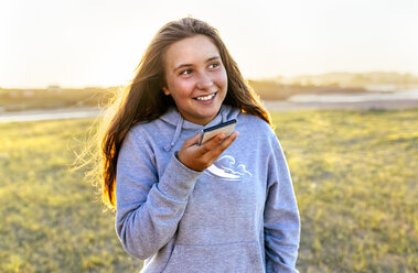Porträt eines lächelnden Mädchens, das ein Mobiltelefon im Freien benutzt - MGOF03680