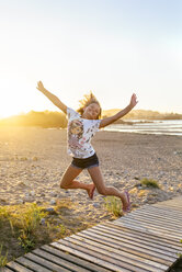 Portrait of smiling girl jumping in the air on the beach - MGOF03688