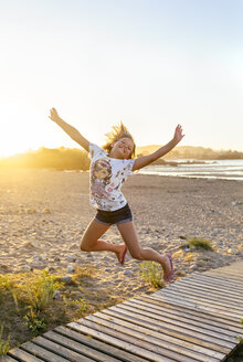 Porträt eines lächelnden Mädchens, das am Strand in die Luft springt - MGOF03688