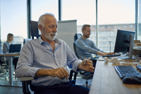 Älterer Geschäftsmann sitzt am Schreibtisch im Büro, lizenzfreies Stockfoto