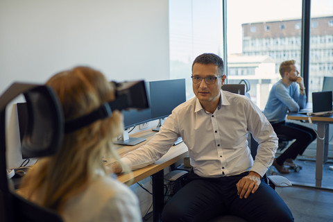 Man looking at woman wearing VR glasses in office stock photo