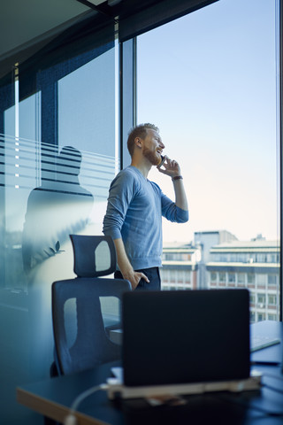 Geschäftsmann im Büro mit Handy am Fenster, lizenzfreies Stockfoto