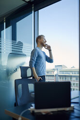 Geschäftsmann im Büro mit Handy am Fenster - ZEDF00959