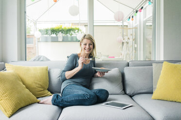 Porträt einer glücklichen Frau, die sich auf der Couch entspannt - MOEF00243