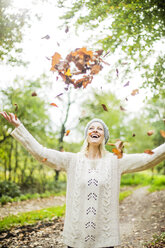 Glückliche Frau im Wald im Herbst wirft Blätter in die Luft - MOEF00258