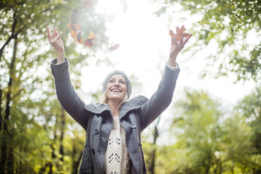 Happy woman in the forest in autumn throwing leaves in the air - MOEF00259