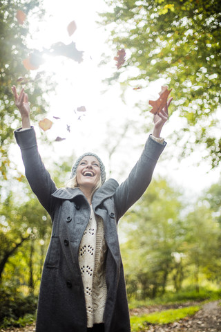 Glückliche Frau im Wald im Herbst wirft Blätter in die Luft, lizenzfreies Stockfoto