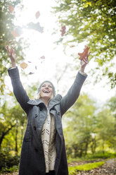 Happy woman in the forest in autumn throwing leaves in the air - MOEF00261