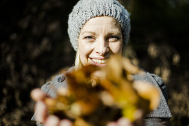 Porträt einer glücklichen Frau im Wald im Herbst, die Blätter hält - MOEF00264