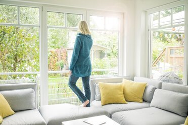 Frau im Wohnzimmer schaut aus dem Fenster - MOEF00270