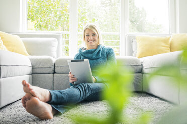 Portrait of happy woman with tablet in living room - MOEF00272
