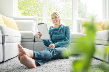 Happy woman using tablet in living room - MOEF00273