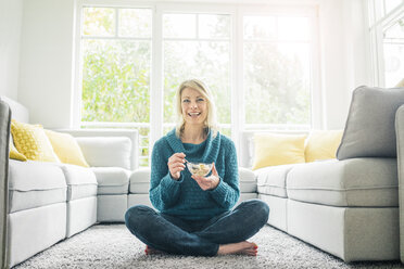 Porträt einer glücklichen Frau, die im Wohnzimmer ein Müsli isst - MOEF00276