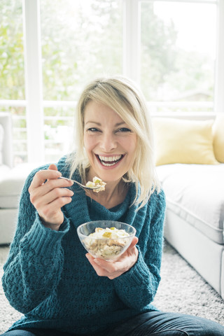 Porträt einer glücklichen Frau, die im Wohnzimmer ein Obstmüsli isst, lizenzfreies Stockfoto