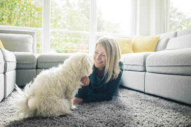 Lächelnde Frau, die ihren Hund im Wohnzimmer streichelt - MOEF00283