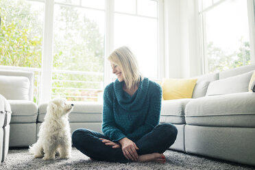 Lächelnde Frau sieht ihren Hund im Wohnzimmer an - MOEF00284